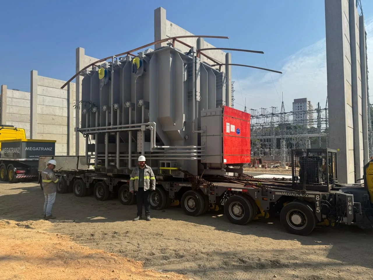Transformador de potência sobre carreta modular no canteiro de uma subestação, com profissionais de EPI